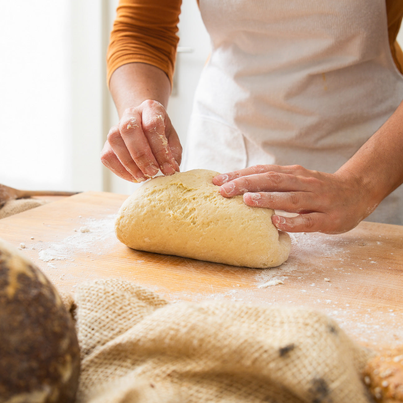Frau mit weißer kochschürze backt Brot und knetet den teig